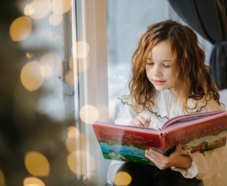 child reading a book by the christmas tree